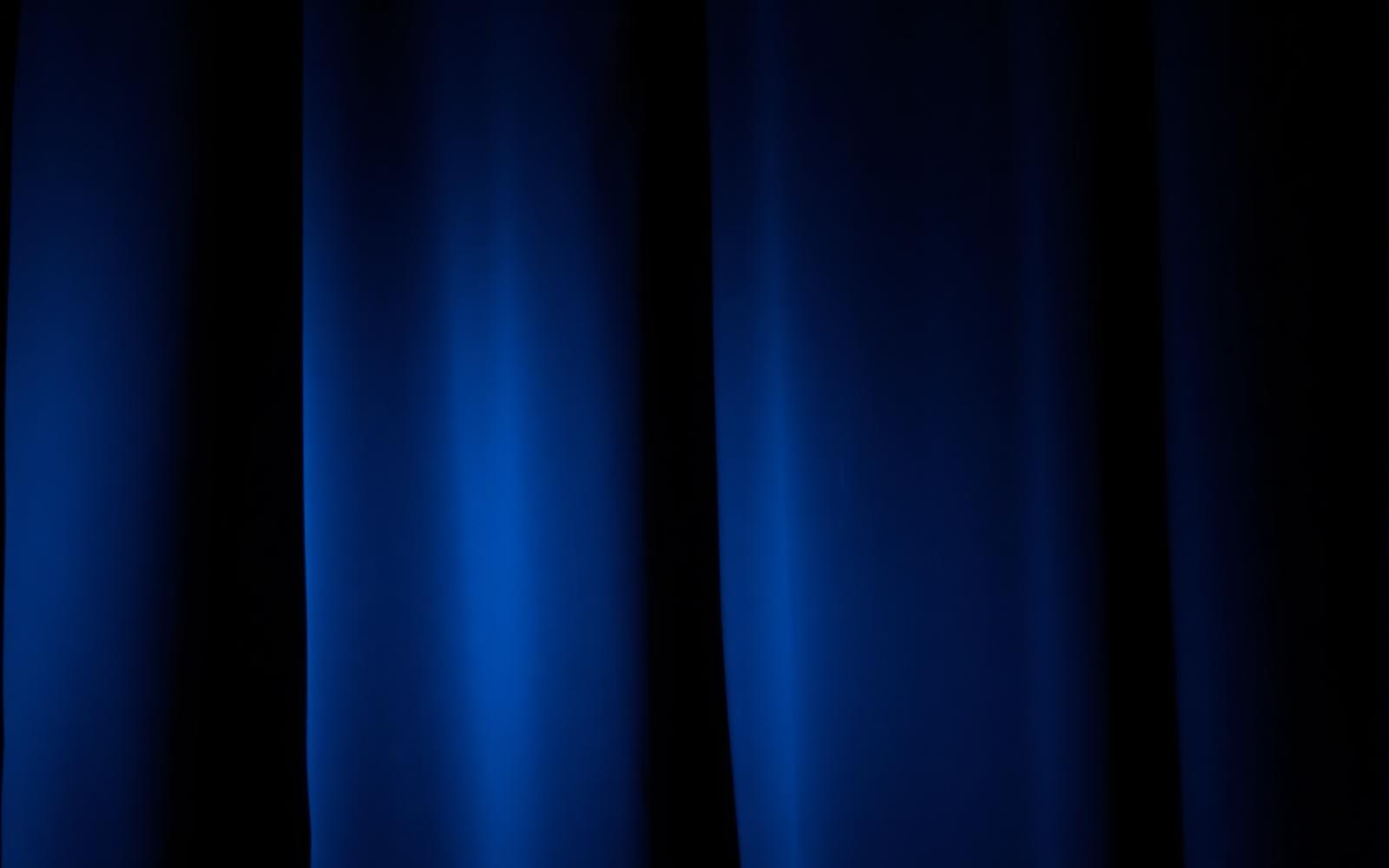 Folds of a dark theatre curtain in low light